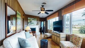 A spacious living room with a white sofa, a floral armchair, a television, and a fireplace.