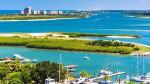A marina with boats docked, surrounded by lush greenery and a clear blue sea.