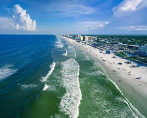 A coastal beach with a long stretch of sand, waves, and a row of buildings along the shore.