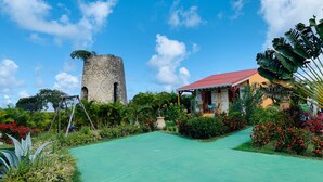 Un giardino con una torre in pietra, una casa dal tetto rosso e diverse piante e fiori.