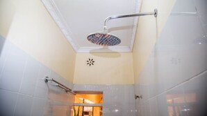 Un pommeau de douche avec un manche incurvé, un mur recouvert de carreaux blancs et une petite fenêtre donnant sur le paysage.