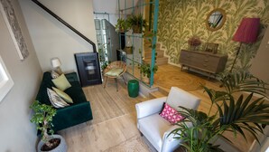 A modern living room with a green sofa, a white armchair, and a staircase with a green railing.
