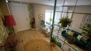 A modern living room with a green sofa, a wicker chair, and various potted plants.