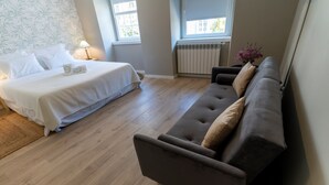 A bedroom with a bed, a sofa, a window, and a radiator.