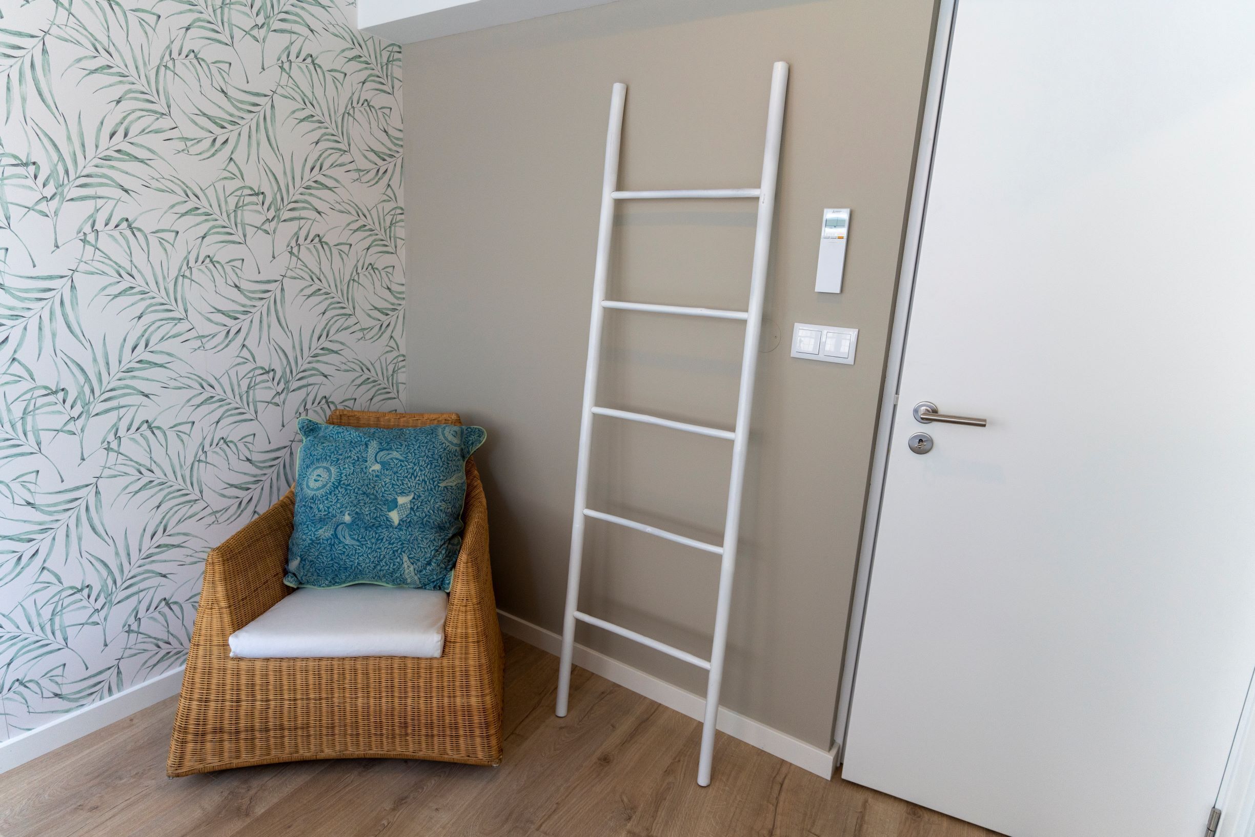 Una habitación con una silla de mimbre, una puerta blanca y una escalera blanca.