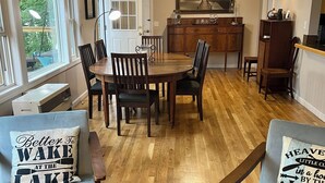 Uma sala de estar ampla com uma mesa de jantar de madeira, duas poltronas cinzas e um tapete estampado.