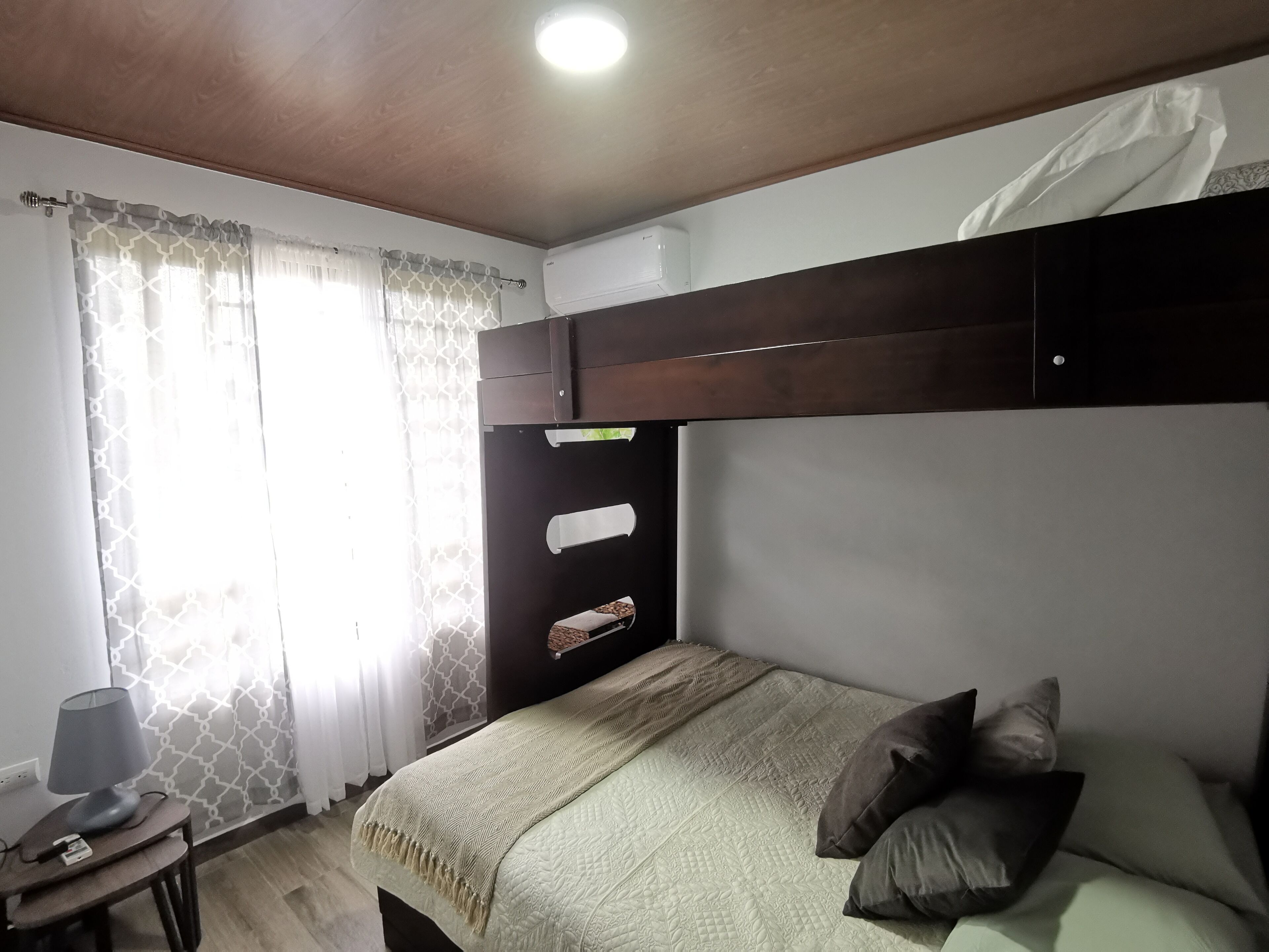 Een slaapkamer met een bed, nachtkastje, lamp en een raam met gordijnen.
