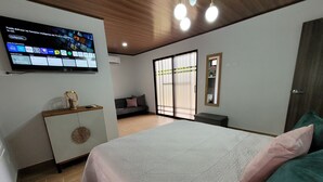 Una camera da letto moderna con un letto grande, una TV a parete, un divano e una porta scorrevole in vetro.