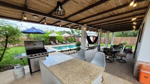 Patio esterno con barbecue, zona salotto e piscina sullo sfondo.