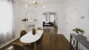 Un coin repas avec une table blanche, des chaises marron, un lustre et une cheminée.