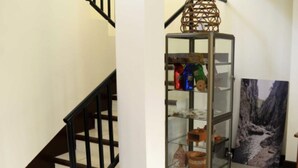 Uma escada com corrimão preto, um expositor de vidro com vários objetos e um quadro grande na parede.