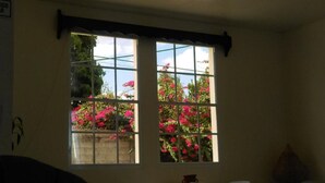 Quarto com uma janela grande com padrão de grade, oferecendo vista de flores cor-de-rosa lá fora.