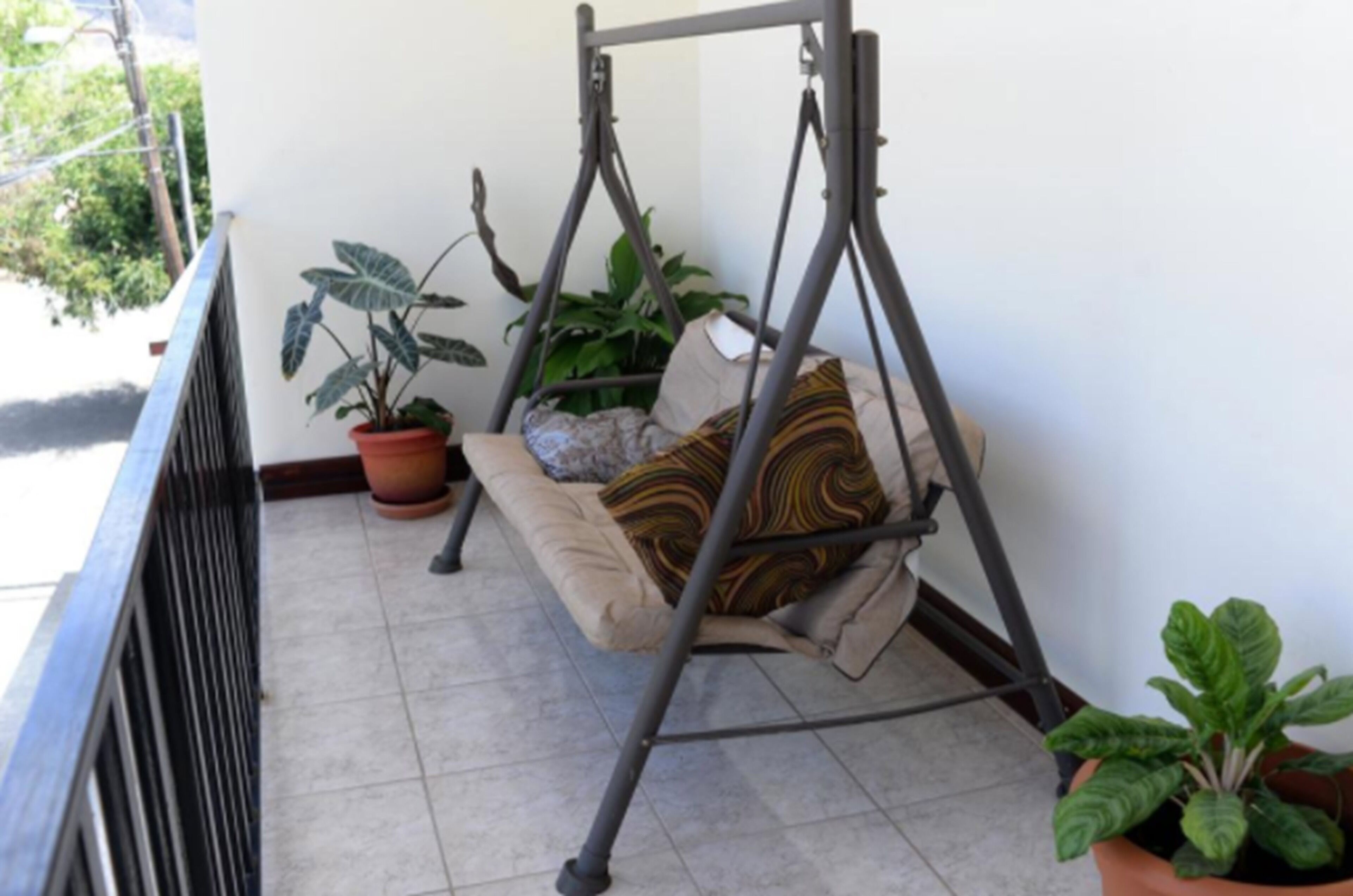 Uma varanda com cadeira de balanço, plantas em vasos e piso de azulejos.