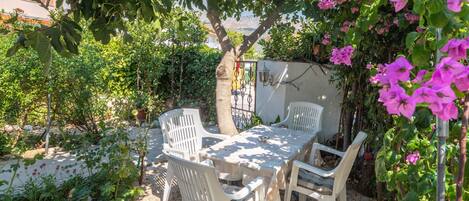 A garden patio with a table and chairs, surrounded by greenery and flowering plants.
