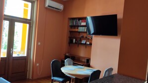 A room with a dining table, chairs, a bookshelf, a flat-screen TV, and an air conditioning unit. - 50m vom Meer entfernt (Lovran)
