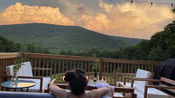 Eine Terrasse mit Sitzgelegenheit, Grill und Blick auf eine bewaldete Berglandschaft.