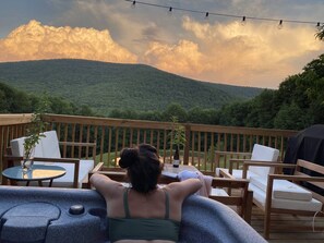 A deck with outdoor seating, a grill, and a view of a forested mountain range.
