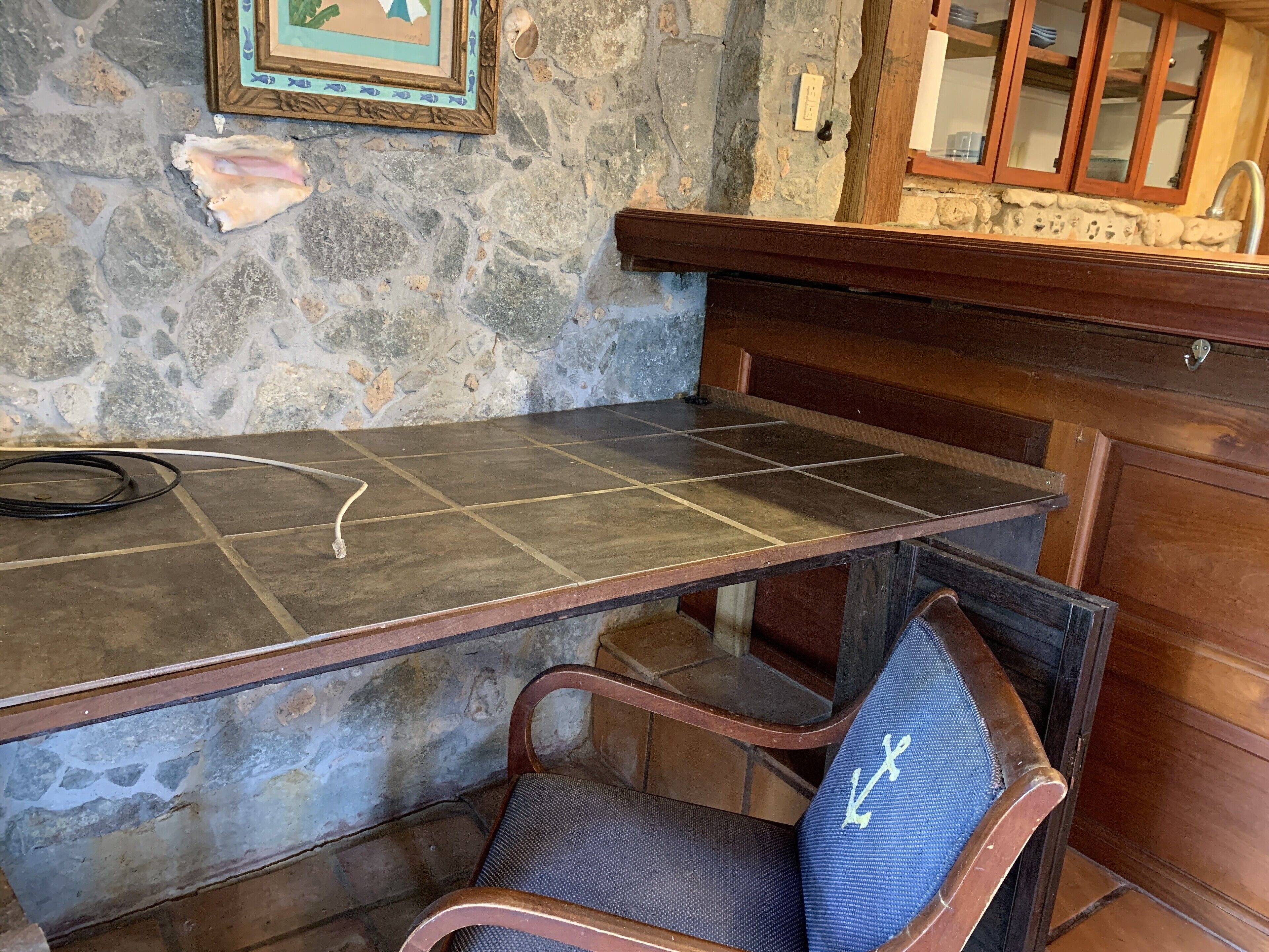 A stone wall, a wooden bar counter, and a chair with a blue cushion.