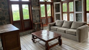 Quarto aconchegante com parede de pedra, móveis de madeira e grandes janelas com vista para o verde.
