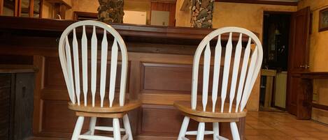 Zwei weiße Adirondack-Stühle mit Holzsitzen und -lehnen, vor einer Bar mit Steinplattenböden und einer Holztresen.