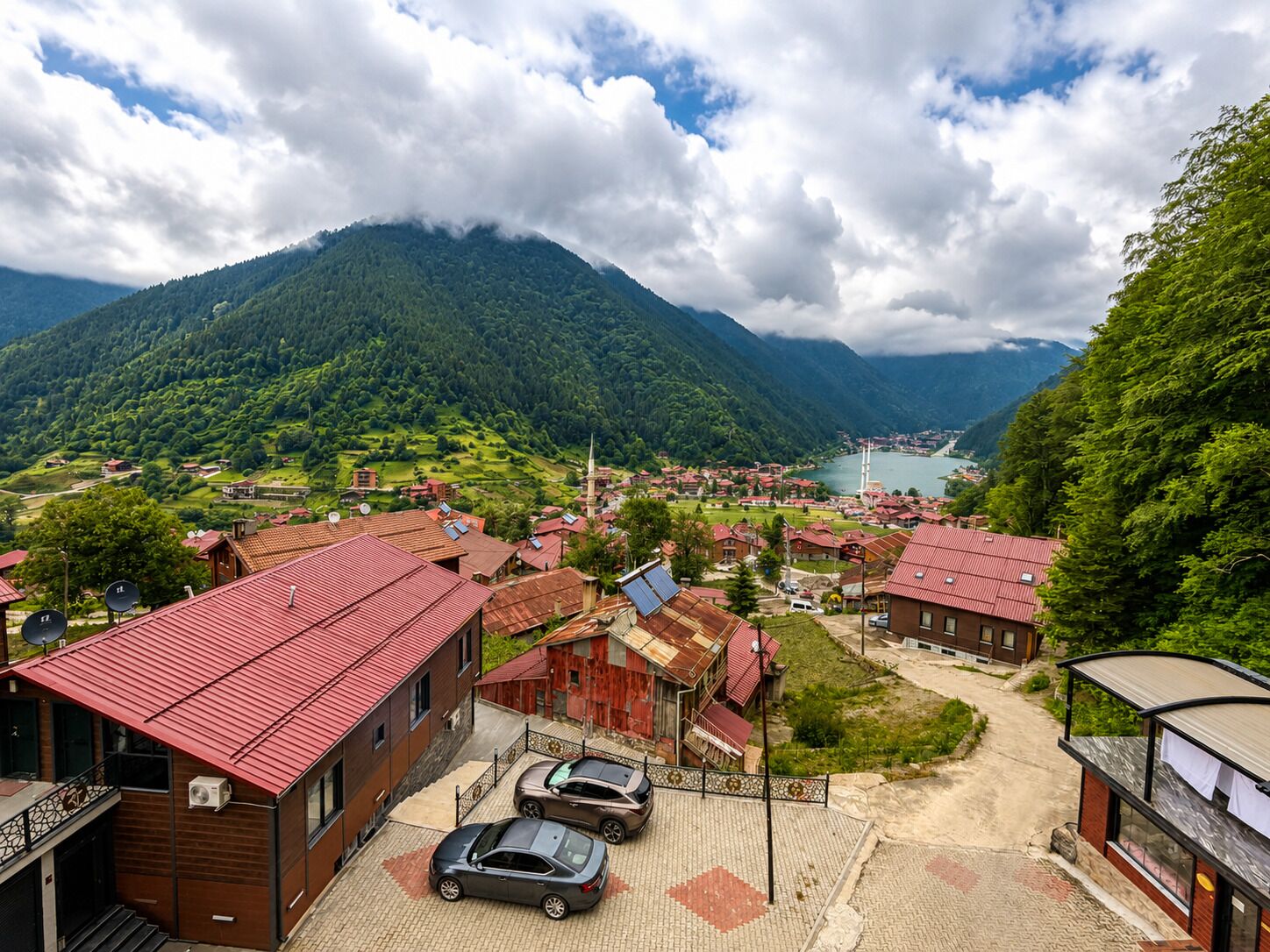 A mountainous landscape with a village, buildings with red roofs, and a lake in the distance.