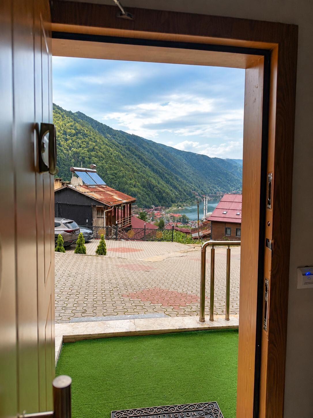 A hotel entrance with a view of a mountainous landscape and a paved area with a green lawn.
