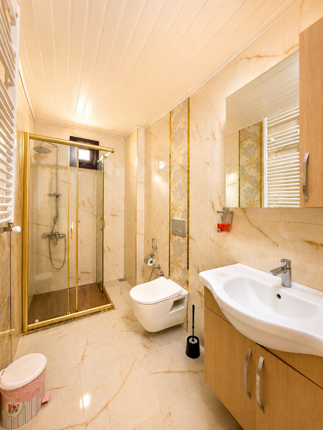 Un baño moderno con ducha de vidrio, inodoro blanco, lavabo con espejo y muebles de madera.