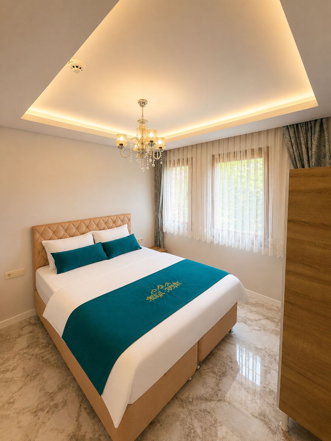 Un dormitorio con cama, candelabro, ventana con cortinas y armario de madera.