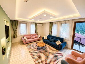 A modern living room with two sofas, a coffee table, and a view of a mountainous landscape through a large window. - Auga Apart (Çaykara)