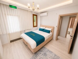 Une chambre d’hôtel avec un lit, un lustre, un appareil de climatisation et une porte donnant sur une autre pièce.