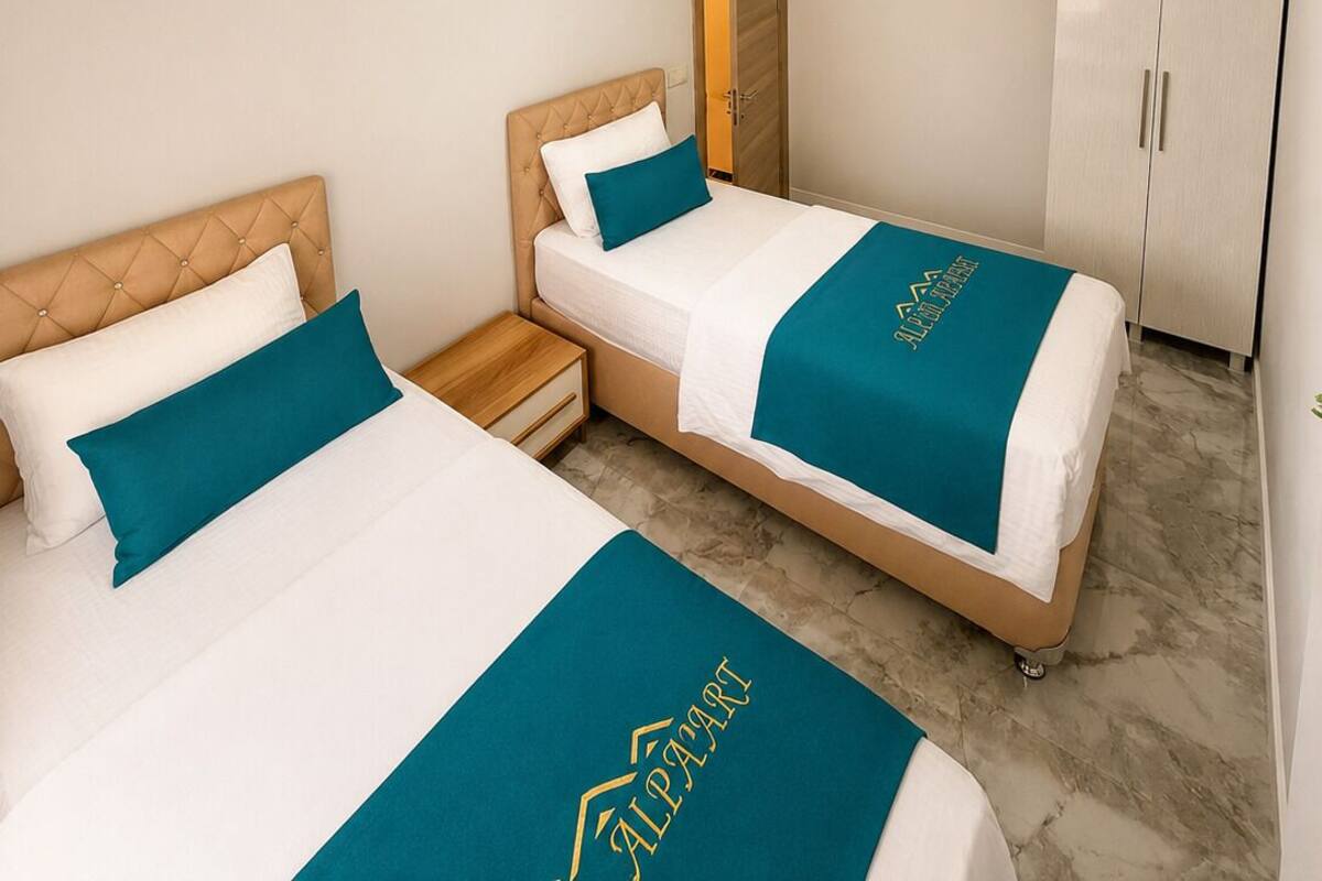 A hotel room with two beds, a wardrobe, a nightstand, and a ceiling light fixture.