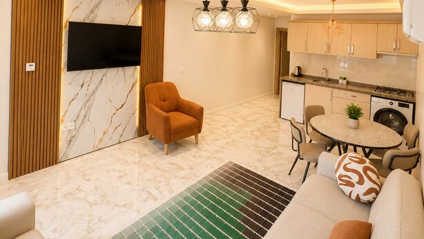 Una sala moderna con un sofá, un televisor montado en la pared, un comedor con mesa y sillas, y una cocina con armarios y electrodomésticos.
