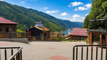 A paved area with a metal railing, a building with a red roof, and a mountain backdrop.