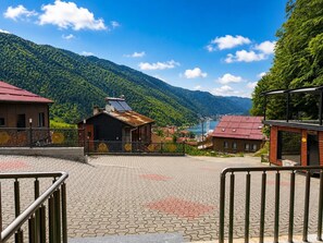 A paved area with a metal railing, a building with a red roof, and a mountain backdrop. - Auga Apart (Çaykara)