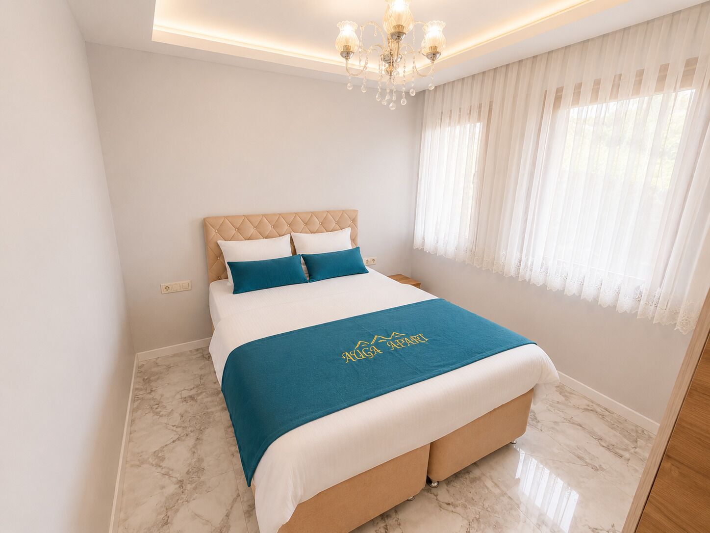 A bedroom with a bed, a chandelier, a window with curtains, and a marble floor.