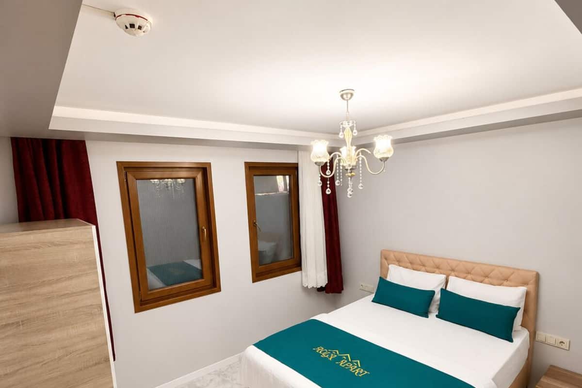 Un dormitorio con cama, armario, araña y ventana con cortinas.