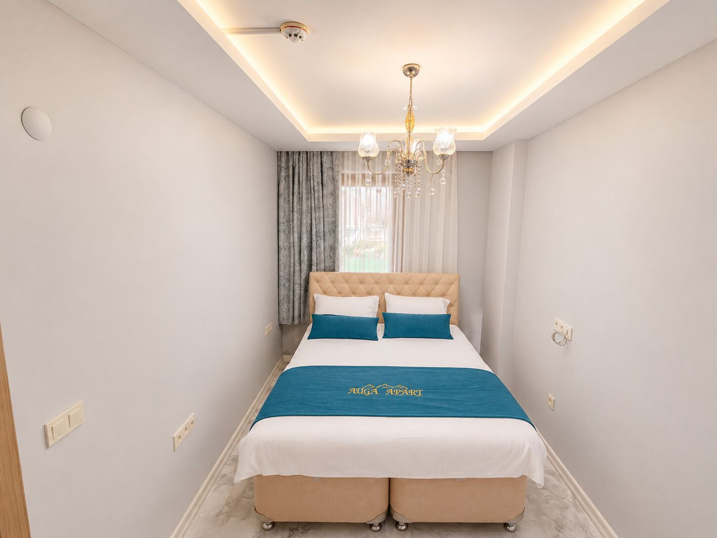 A modern bedroom with a tufted headboard, a bed with a teal bedspread, and a chandelier.