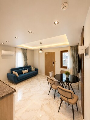 A modern living room with a blue sofa, a dining table with chairs, and a ceiling light fixture.