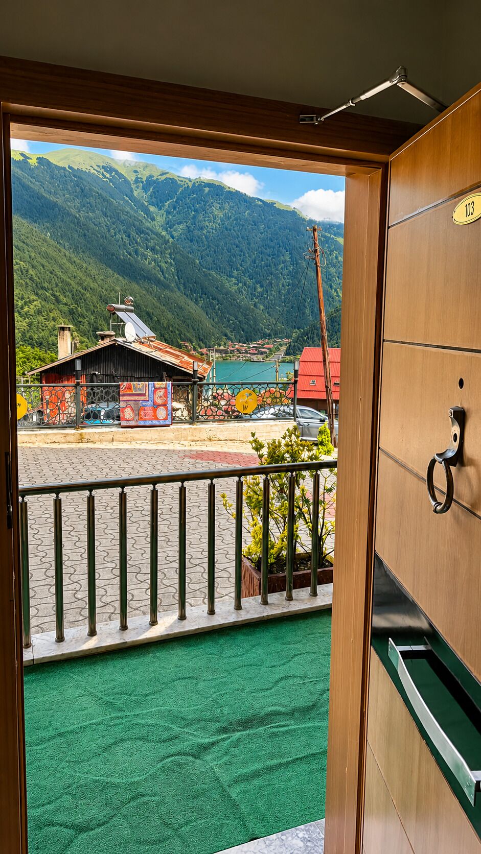 A room with a view of a mountain landscape, a balcony with a railing, and a door with a handle.