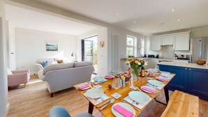 A modern kitchen with white cabinets, a dining area with a wooden table set for six, and a grey sofa in the living area. - Beautifully refurbished holiday home in the centre of Abersoch with parking. (Abersoch)