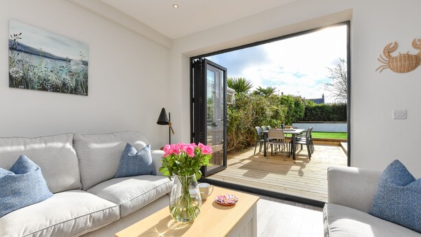 A modern living room with a sofa, a coffee table with a vase of flowers, and a view of an outdoor patio area with a table and chairs. - Beautifully refurbished holiday home in the centre of Abersoch with parking. (Abersoch)