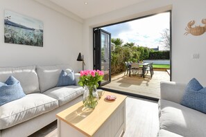 Ein modernes Wohnzimmer mit einer Couch, einem Couchtisch mit Blumenvase und Blick auf eine Außenpatio-Terrasse mit Tisch und Stühlen.