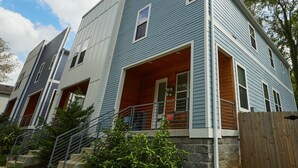 Un immeuble résidentiel de deux étages, doté de fondations en pierre, d’une terrasse en bois et d’un escalier métallique menant à l’entrée.