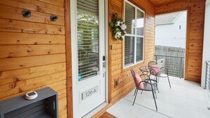 Une façade en bois avec une porte blanche portant l’inscription « 126 A », une petite table avec des chaises et une fenêtre agrémentée d’un arrangement floral blanc.