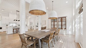 A spacious dining area with a long wooden table, wicker chairs, and two large white pendant lights.