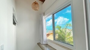 Un pasillo estrecho con techo de madera, lámpara colgante, ventana con vista a palmeras y una playa, y un banco empotrado.