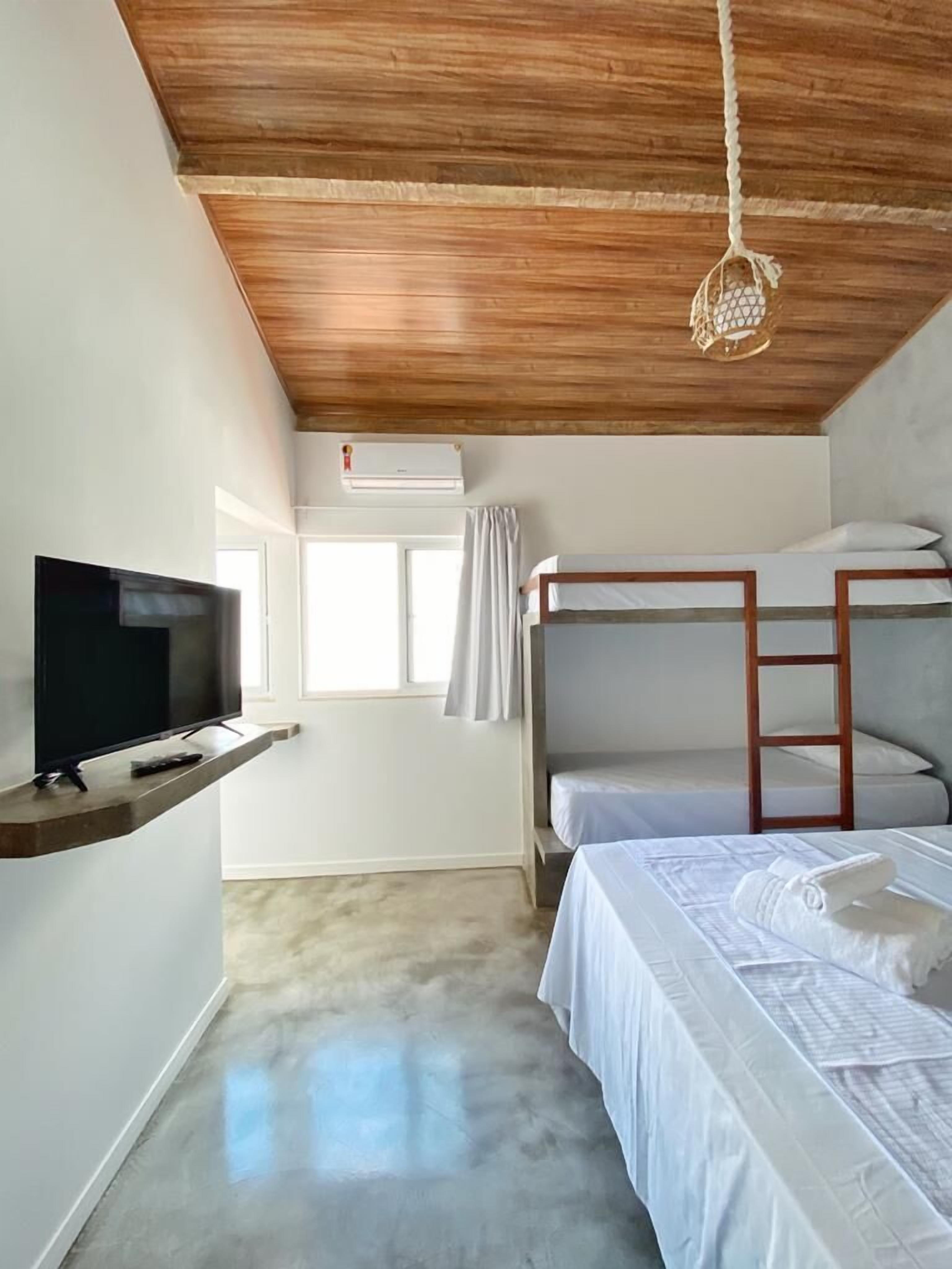 Une chambre avec des lits superposés, un téléviseur posé sur une étagère et un luminaire suspendu au plafond.