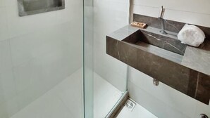 Un baño moderno con cabina de ducha de vidrio, lavamanos de mármol y espejo montado en la pared.