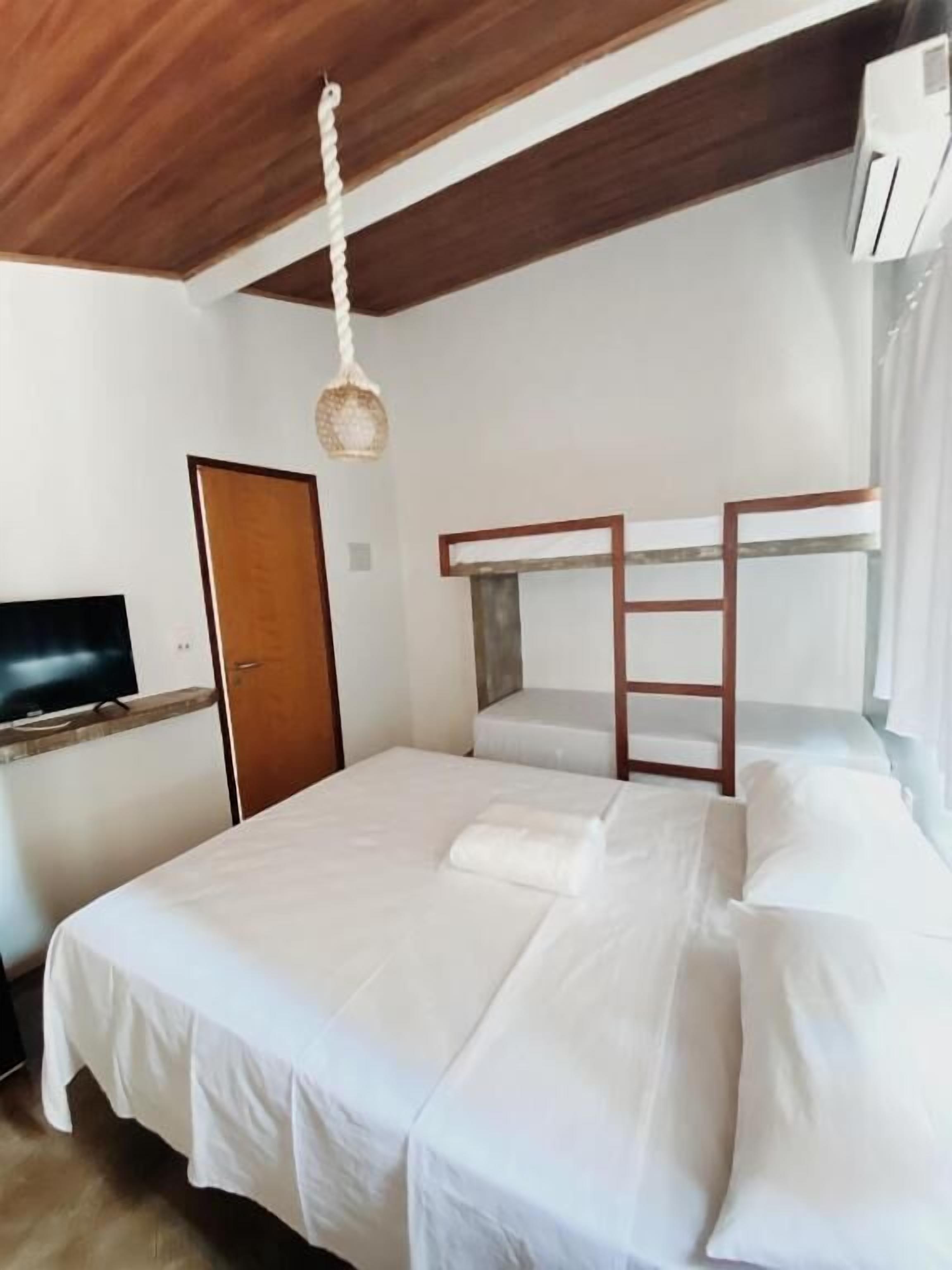 A single-bed room with a wooden bunk bed, a television on a shelf, and a hanging light fixture.