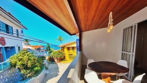 Un balcón con techo de madera, una mesa de comedor con sillas blancas y vistas a edificios vecinos.